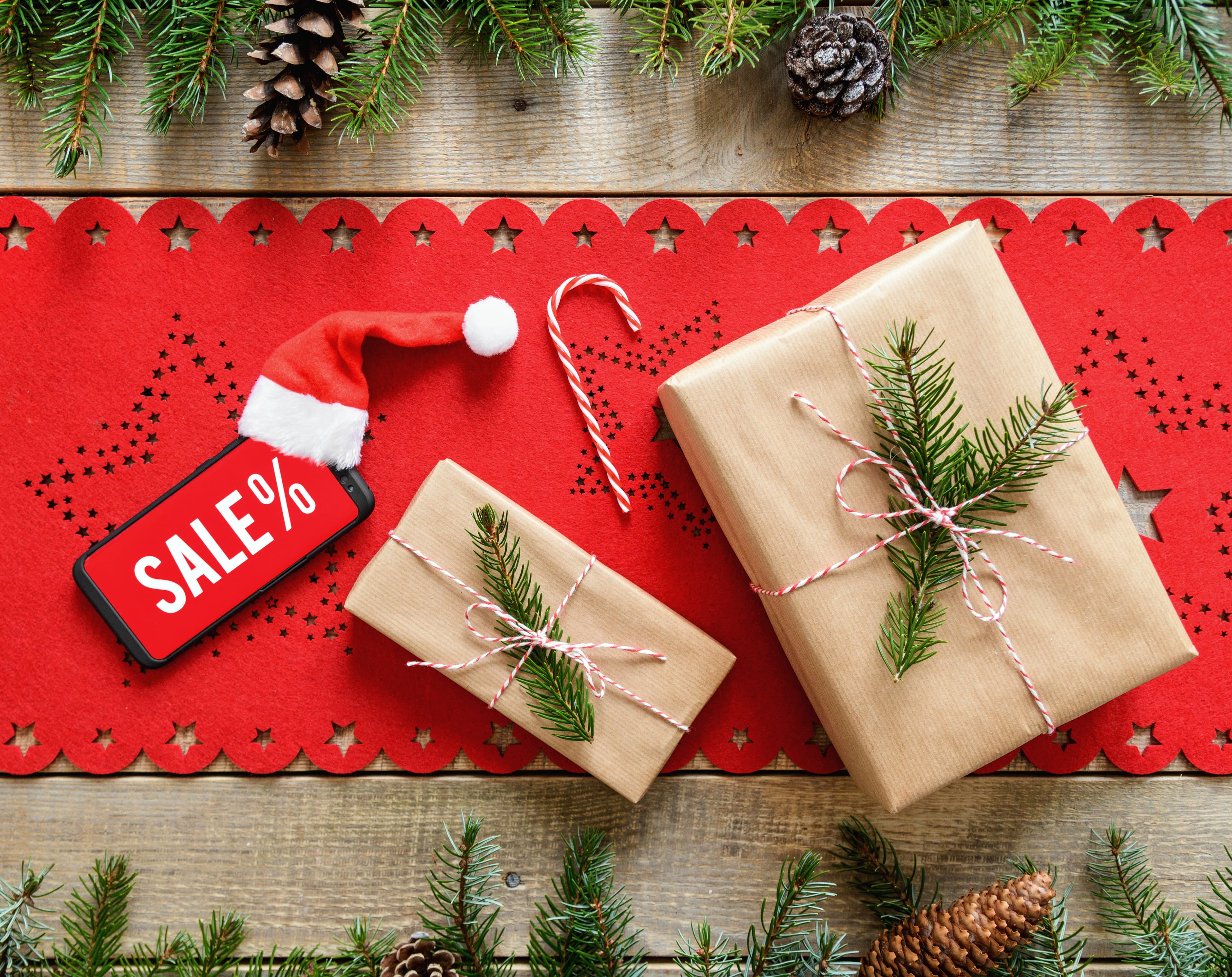 Top view of a wooden surface with a red Christmas table cloth a smartphone indicating Christmas sale
